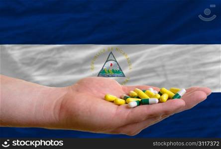 man holding capsules in front of complete wavy national flag of nicaragua symbolizing health, medicine, cure, vitamines and healthy life