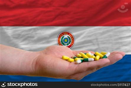 man holding capsules in front of complete wavy national flag of paraguay symbolizing health, medicine, cure, vitamines and healthy life