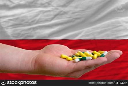 man holding capsules in front of complete wavy national flag of poland symbolizing health, medicine, cure, vitamines and healthy life