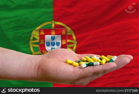 man holding capsules in front of complete wavy national flag of portugal symbolizing health, medicine, cure, vitamines and healthy life