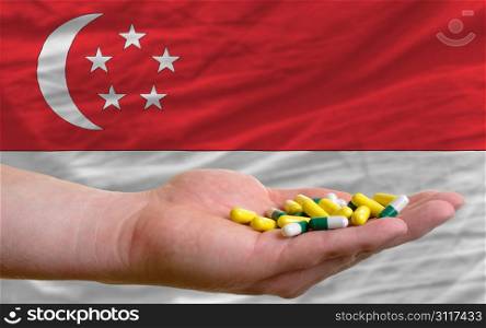 man holding capsules in front of complete wavy national flag of singapore symbolizing health, medicine, cure, vitamines and healthy life