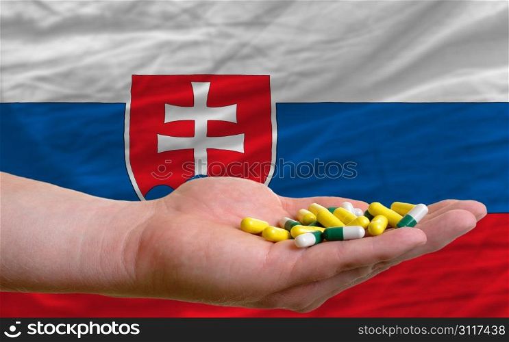 man holding capsules in front of complete wavy national flag of slovakia symbolizing health, medicine, cure, vitamines and healthy life