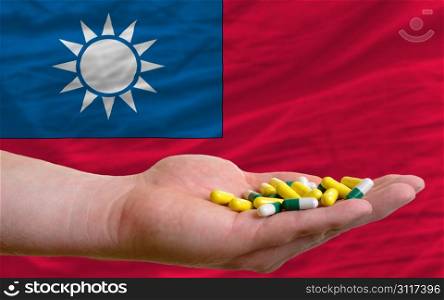 man holding capsules in front of complete wavy national flag of taiwan symbolizing health, medicine, cure, vitamines and healthy life