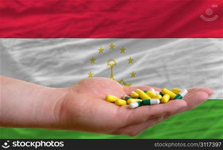 man holding capsules in front of complete wavy national flag of tajikistan symbolizing health, medicine, cure, vitamines and healthy life