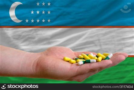 man holding capsules in front of complete wavy national flag of uzbekistan symbolizing health, medicine, cure, vitamines and healthy life