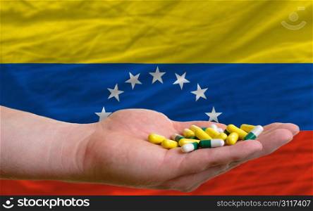 man holding capsules in front of complete wavy national flag of venezuela symbolizing health, medicine, cure, vitamines and healthy life