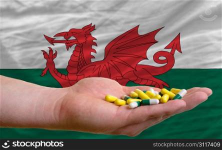 man holding capsules in front of complete wavy national flag of wales symbolizing health, medicine, cure, vitamines and healthy life