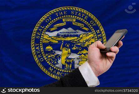 man holding cell phone in front flag of us state of nebraska symbolizing mobile communication and telecommunication