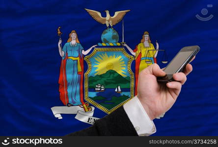 man holding cell phone in front flag of us state of new york symbolizing mobile communication and telecommunication