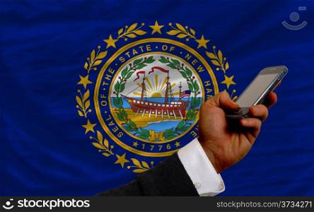 man holding cell phone in front flag of us state of new hampshire symbolizing mobile communication and telecommunication