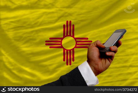 man holding cell phone in front flag of us state of new mexico symbolizing mobile communication and telecommunication