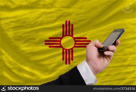 man holding cell phone in front flag of us state of new mexico symbolizing mobile communication and telecommunication