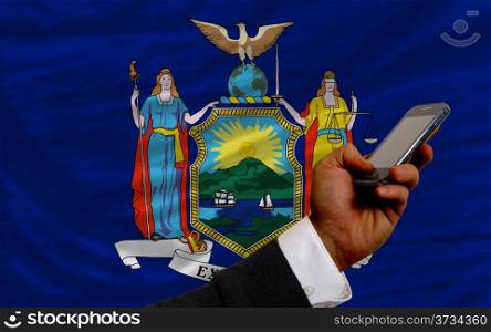 man holding cell phone in front flag of us state of new york symbolizing mobile communication and telecommunication