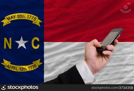 man holding cell phone in front flag of us state of north carolina symbolizing mobile communication and telecommunication