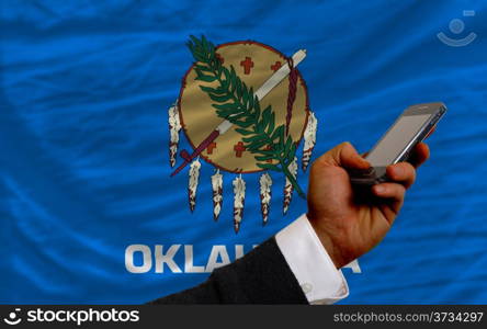 man holding cell phone in front flag of us state of oklahoma symbolizing mobile communication and telecommunication