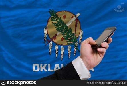 man holding cell phone in front flag of us state of oklahoma symbolizing mobile communication and telecommunication