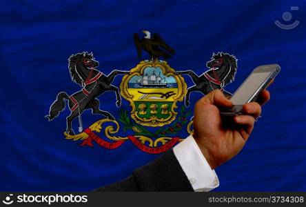 man holding cell phone in front flag of us state of pennsylvania symbolizing mobile communication and telecommunication