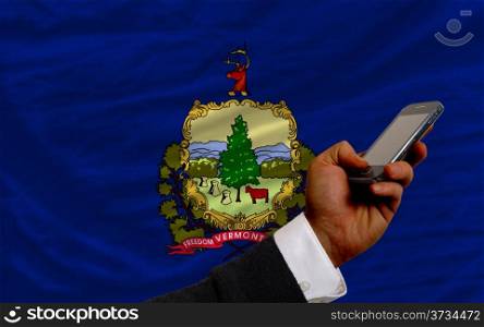man holding cell phone in front flag of us state of vermont symbolizing mobile communication and telecommunication