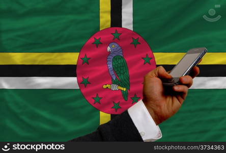 man holding cell phone in front national flag of dominica symbolizing mobile communication and telecommunication