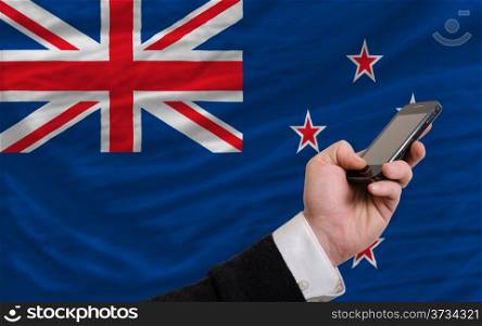 man holding cell phone in front national flag of new zealand symbolizing mobile communication and telecommunication