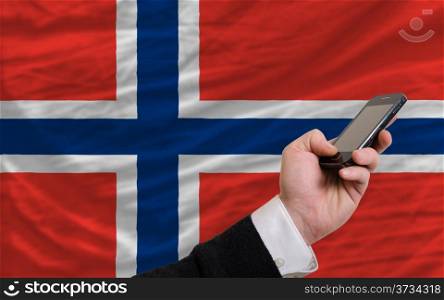 man holding cell phone in front national flag of norway symbolizing mobile communication and telecommunication