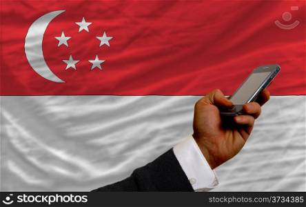 man holding cell phone in front national flag of singapore symbolizing mobile communication and telecommunication
