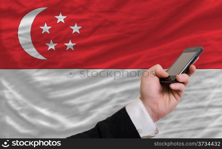 man holding cell phone in front national flag of singapore symbolizing mobile communication and telecommunication