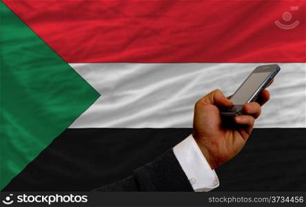 man holding cell phone in front national flag of sudan symbolizing mobile communication and telecommunication