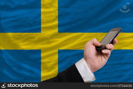 man holding cell phone in front national flag of sweden symbolizing mobile communication and telecommunication