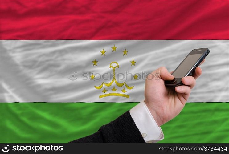 man holding cell phone in front national flag of tajikistan symbolizing mobile communication and telecommunication