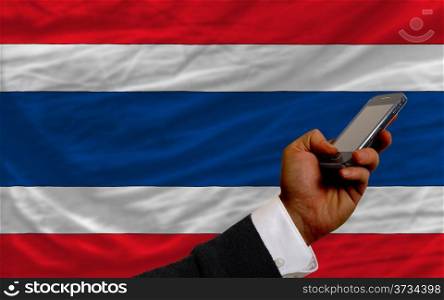 man holding cell phone in front national flag of thailand symbolizing mobile communication and telecommunication