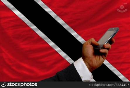 man holding cell phone in front national flag of trinidad tobago symbolizing mobile communication and telecommunication