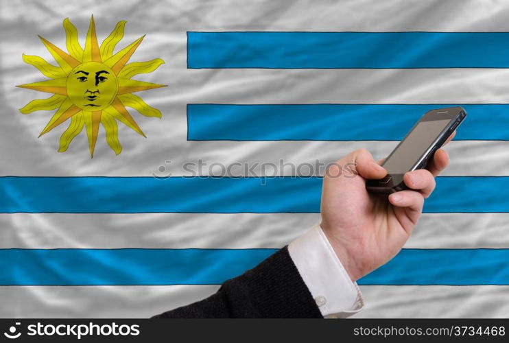 man holding cell phone in front national flag of uruguay symbolizing mobile communication and telecommunication