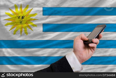 man holding cell phone in front national flag of uruguay symbolizing mobile communication and telecommunication