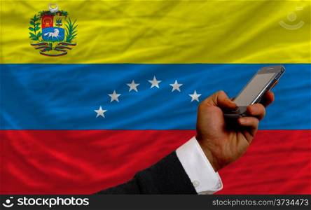 man holding cell phone in front national flag of venezuela symbolizing mobile communication and telecommunication