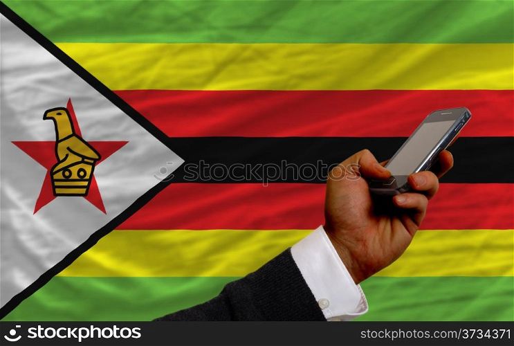 man holding cell phone in front national flag of zimbabwe symbolizing mobile communication and telecommunication