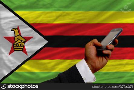 man holding cell phone in front national flag of zimbabwe symbolizing mobile communication and telecommunication