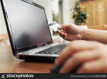 Man holding credit card in hand and entering security code using laptop keyboard