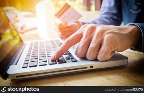 Man holding credit card in hand and entering security code using laptop keyboard.