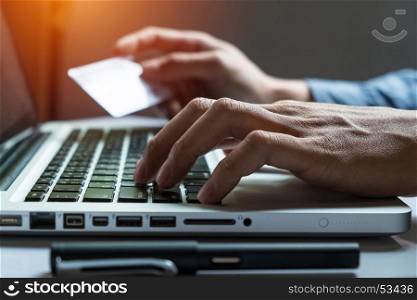Man holding credit card in hand and entering security code using smart phone on laptop keyboard, online shopping concept.