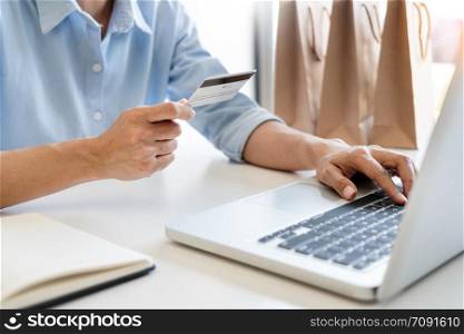 Man holding credit card in hand and entering security code using smart phone on laptop keyboard, online payment shopping concept.