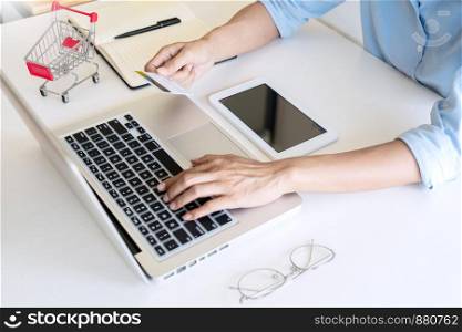 Man holding credit card in hand and entering security code using smart phone on laptop keyboard, online payment shopping concept.