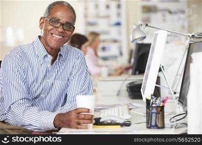 Man Holding Cup Working At Desk In Busy Creative Office