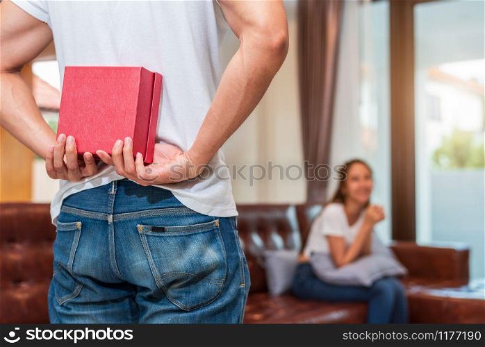Man holding gift behind him for surprise girlfriend at their home. Woman waiting for Valentines gift form boyfriend. Happy Birthday party anniversary concept. People couple lifestyles and family life