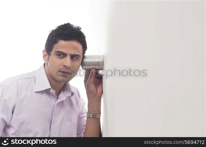 Man holding glass against wall listening