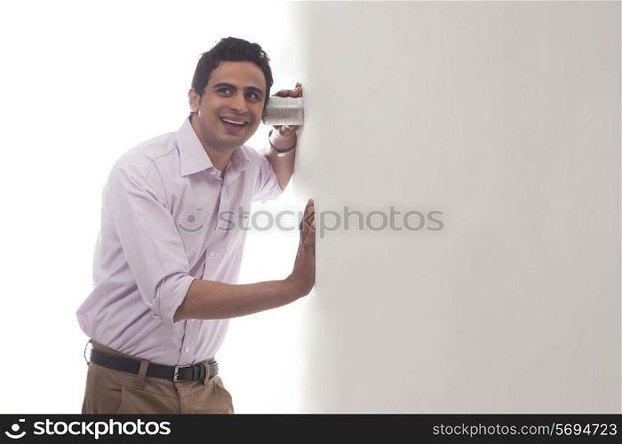 Man holding glass against wall listening