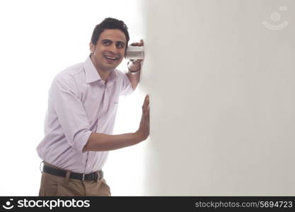 Man holding glass against wall listening