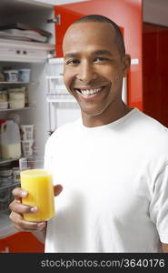 Man holding glass of orange juice, by fridge, portrait