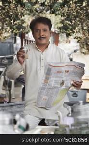 Man holding glass of tea and newspaper looking at camera