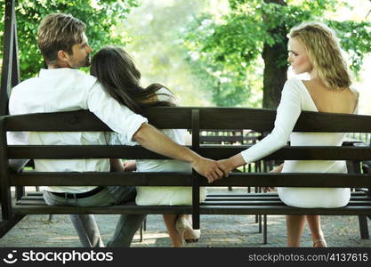 Man holding hands with another woman on a bench.